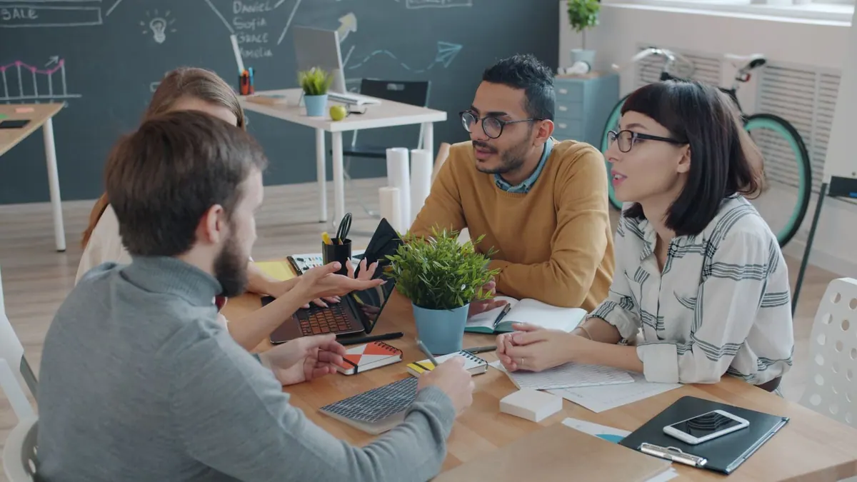 Equipe diversa colaborando em uma mesa de reunião com laptop e gráficos.