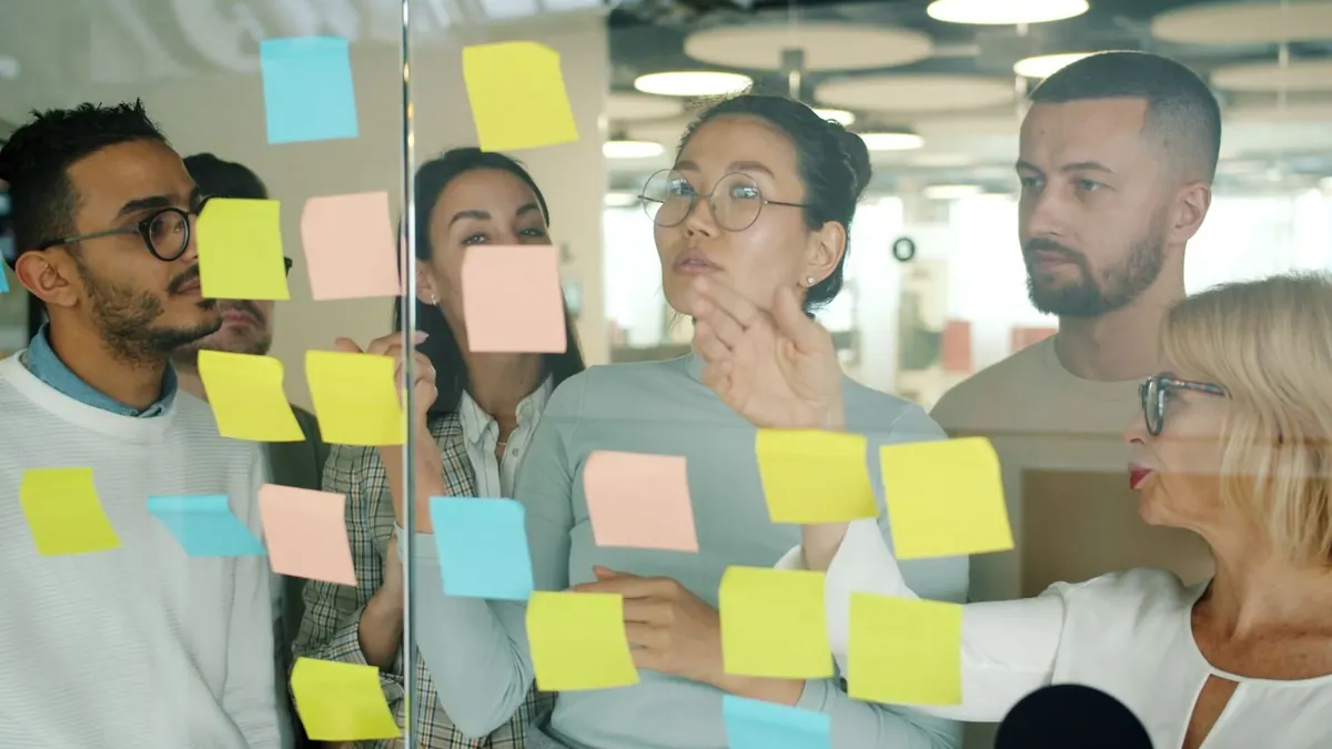 Equipe diversa colaborando com post-its em um quadro de vidro no escritório.