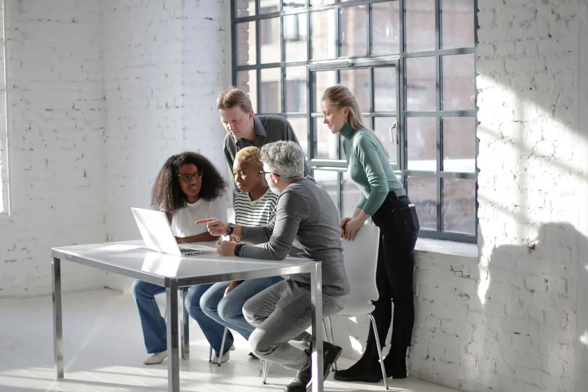 Grupo diverso de colegas de trabalho colaborando em um laptop em um escritório moderno.