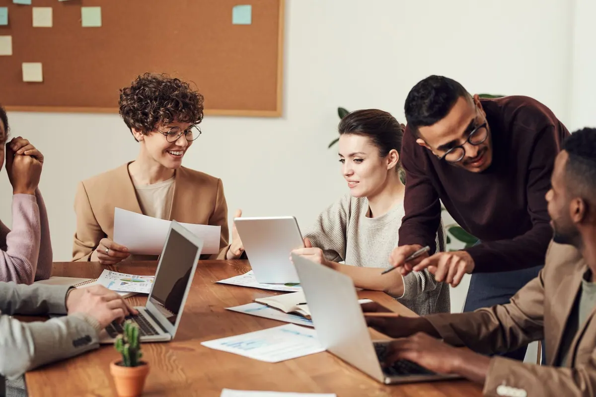 Pessoas diversas colaborando em uma mesa de reunião com laptops e documentos.