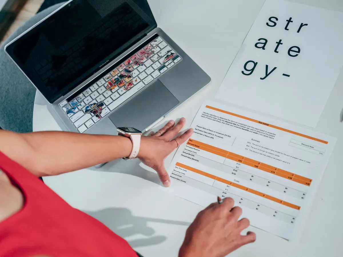Pessoa analisando documentos e um laptop com adesivos coloridos sobre uma mesa branca.