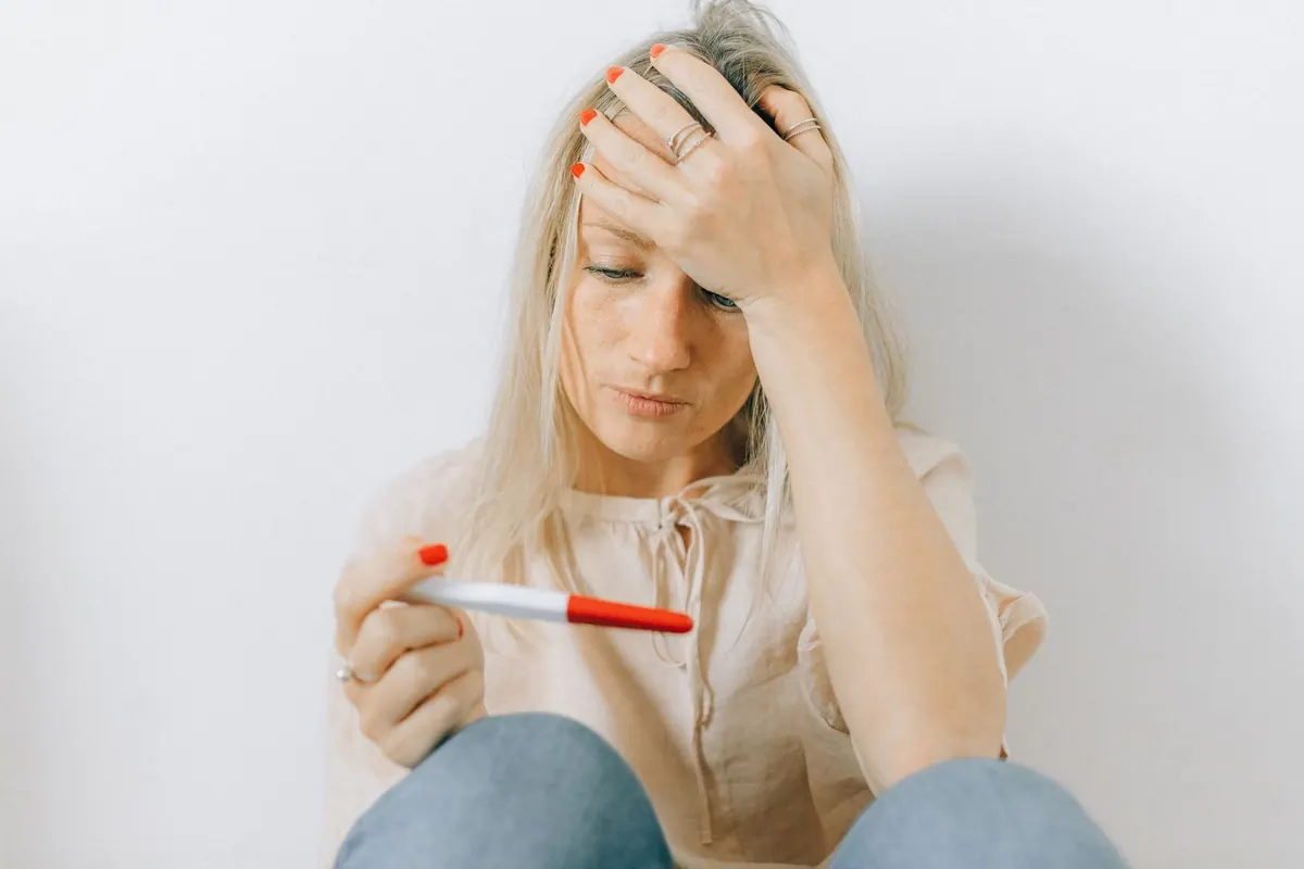 Mulher loira com expressão de tristeza e preocupação segurando um teste de gravidez.