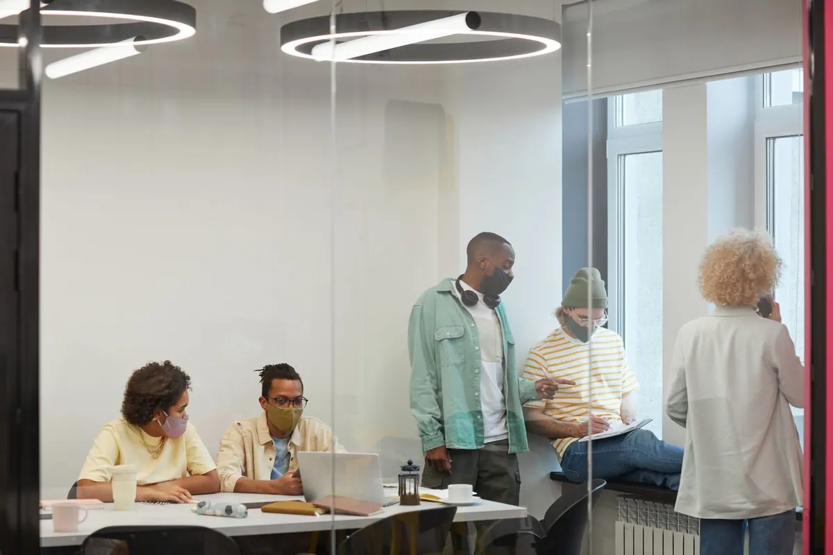 Pessoas usando máscaras em um escritório moderno com paredes de vidro.