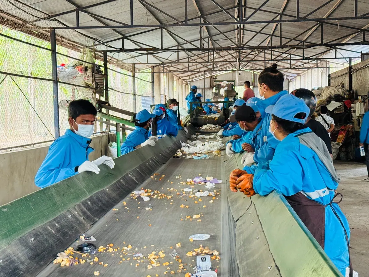 Trabalhadores em uma instalação de reciclagem, separando resíduos em uma esteira.