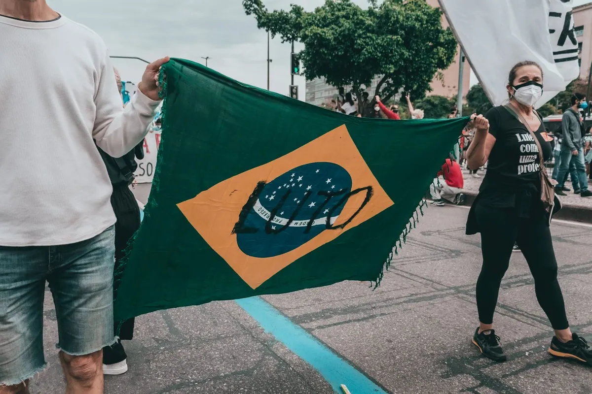 Pessoas segurando a bandeira do Brasil com uma máscara no centro.