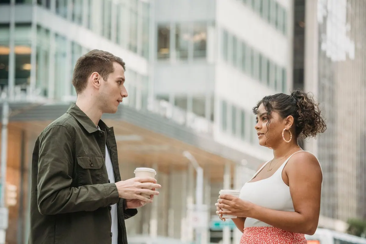 Dois colegas de trabalho jovens conversando e tomando café em ambiente urbano.