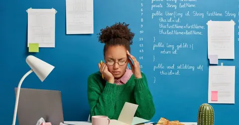Mulher negra em frente ao notebook com as mãos na cabeça como se estivesse com dor