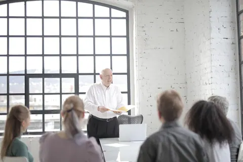 Executivo sênior lidera reunião de equipe em escritório moderno, apresentando ideias.