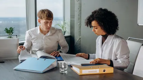 Dois colegas de trabalho, um homem e uma mulher, revisando documentos em um escritório.