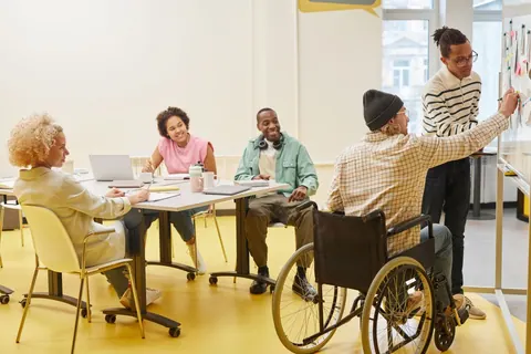 Grupo diverso de pessoas em reunião, incluindo um cadeirante, interagindo e colaborando.