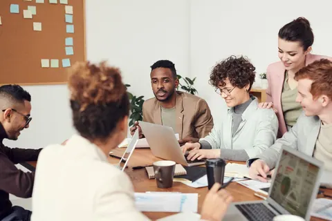 Grupo diverso de profissionais em reunião, colaborando e usando laptops.