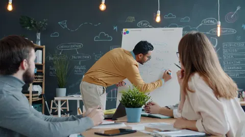 Pessoas colaborando em um escritório moderno, com um homem escrevendo em um quadro branco.