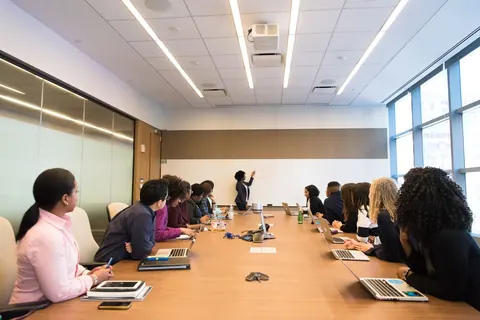 Pessoas em uma sala de conferência, uma delas apresentando em um quadro branco.