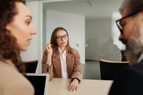 Três pessoas em uma reunião de negócios, uma mulher de óculos no centro.