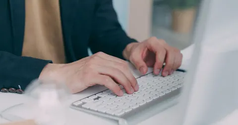 Mãos profissionais digitando em um teclado branco, focando no desenvolvimento de carreira.