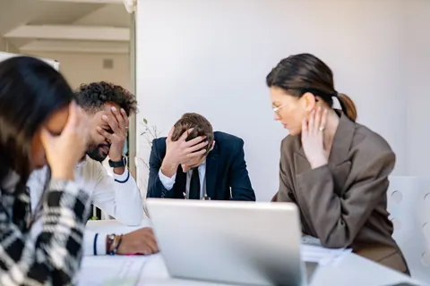 Pessoas de negócios estressadas em um escritório, com as mãos na cabeça.