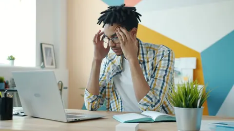 Profissional de RH estressado no escritório com laptop, refletindo sobre desafios.