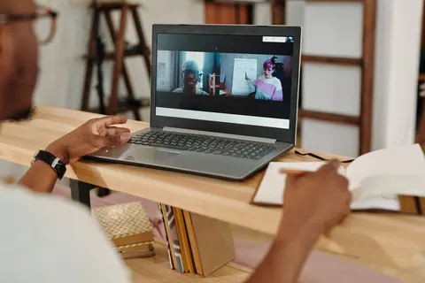 Homem assistindo a uma videochamada em laptop e fazendo anotações.