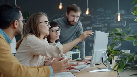 Colegas diversos colaborando em frente a um computador em um escritório moderno.