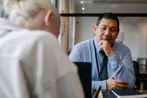 Gerente étnico positivo olhando para cliente sentado no escritório