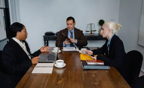 Pessoas em uma reunião de negócios, com um homem no centro e duas mulheres nas laterais.