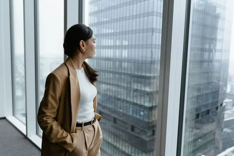 Mulher de negócios pensativa olhando pela janela do escritório, contemplando o futuro.