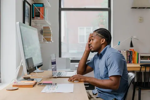 Homem com expressão de cansaço e frustração olhando para a tela do computador.