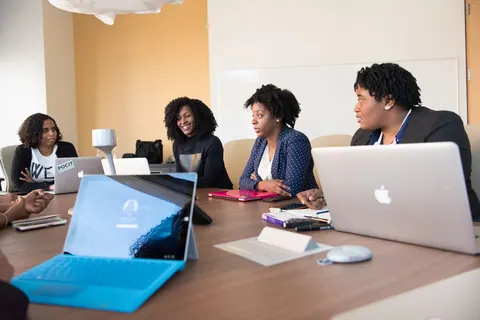 Mulheres diversas em reunião de trabalho com laptops e tablets.