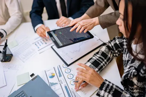 Pessoas analisando dados em um tablet durante uma reunião de trabalho.