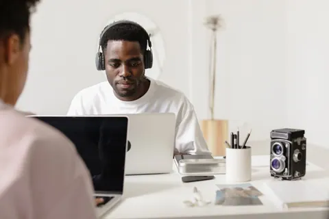 Homem jovem focado, usando fones de ouvido, trabalhando em seu laptop no escritório.