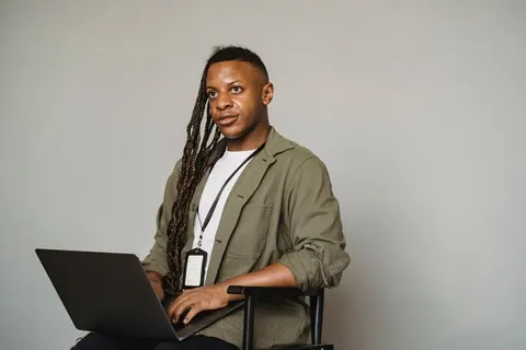 Homem trans negro trabalhando em laptop, representando inclusão e apoio no ambiente de trabalho.