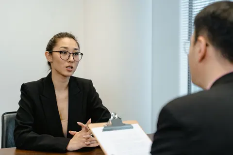 Mulher em entrevista de emprego, olhando para o recrutador com expressão séria.