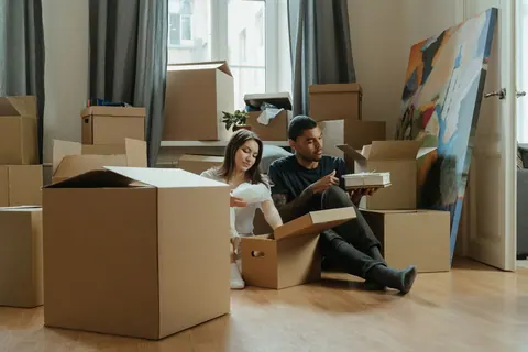 Casal jovem sentado no chão, desempacotando caixas de mudança em uma sala.