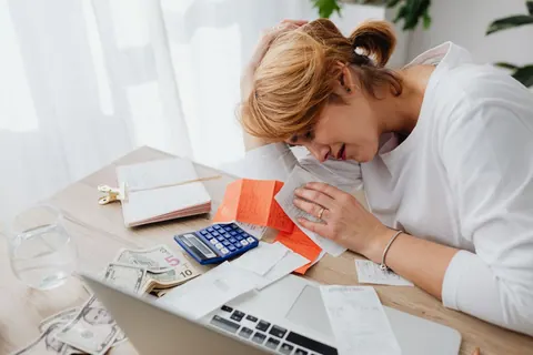 Mulher estressada com contas e recibos na mesa, evidenciando estresse financeiro.