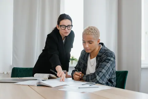Mulher orientando um jovem estudante em uma mesa de escritório.