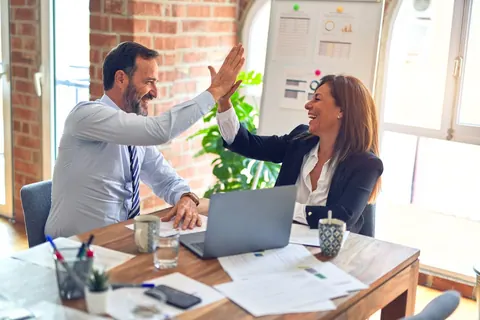 Dois colegas de trabalho sorrindo e batendo as mãos em sinal de comemoração.