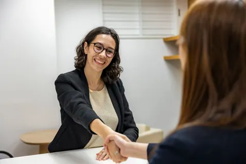 Jovem candidata sorridente cumprimentando recrutadora em entrevista de emprego