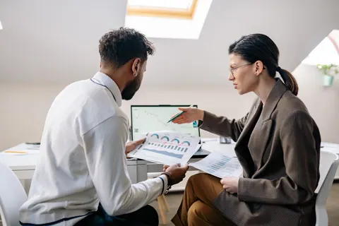 Duas pessoas em reunião de trabalho, analisando gráficos e dados de gestão.