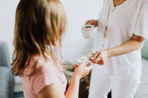 Mãe entregando dinheiro à filha, representando mesada ou poupança.