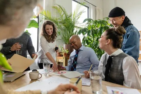 Pessoas diversas em um escritório moderno, sorrindo e interagindo durante uma reunião.