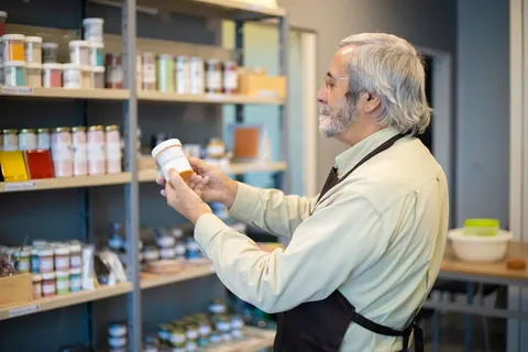 Funcionário grisalho de avental examinando produtos em uma loja