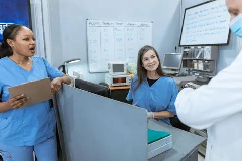 Médico e enfermeiras conversando em ambiente hospitalar, com quadro branco ao fundo.