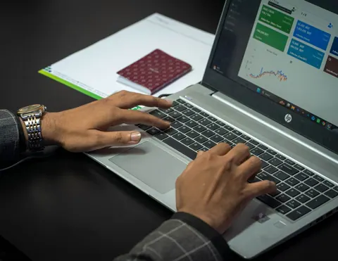 Mãos de um profissional digitando em um laptop exibindo gráficos e dados.
