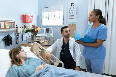 Enfermeira e médico conversando ao lado de paciente em um quarto de hospital.