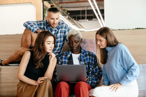 Grupo diverso de colegas de trabalho interagindo e usando um laptop em um ambiente de escritório moderno.