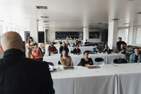 Pessoas em uma sala de treinamento, com um palestrante de costas para a câmera.