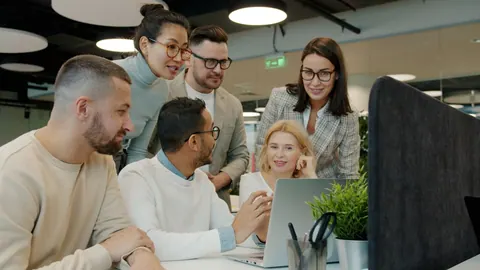 Equipe diversa colaborando em frente a um notebook em um escritório moderno.