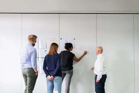 Quatro colegas de trabalho discutem um organograma em um quadro branco.