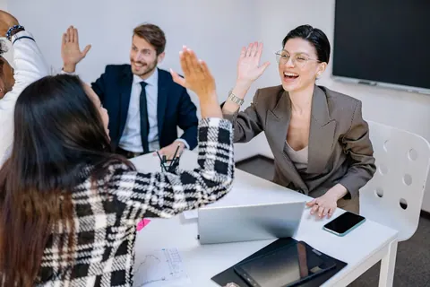 Equipe de trabalho diversa celebrando com high-five em uma sala de reunião.