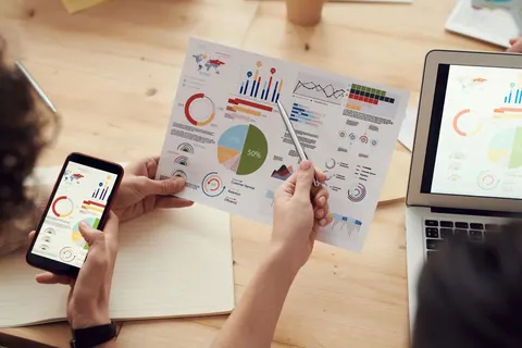 Mãos de pessoas analisando gráficos e dados de uma pesquisa em papel e celular.